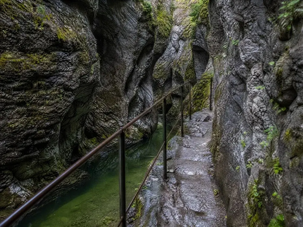 Un sentiero scavato nella roccia con corrimano metallico sopra l'acqua verde